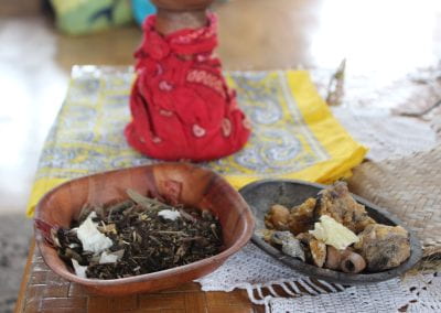 In two separate bowls, a collection of dried herbs and several crystalline objects sit on a table inside, next to a red bandana and a yellow bandana in Tuwaliri's cloud forest
