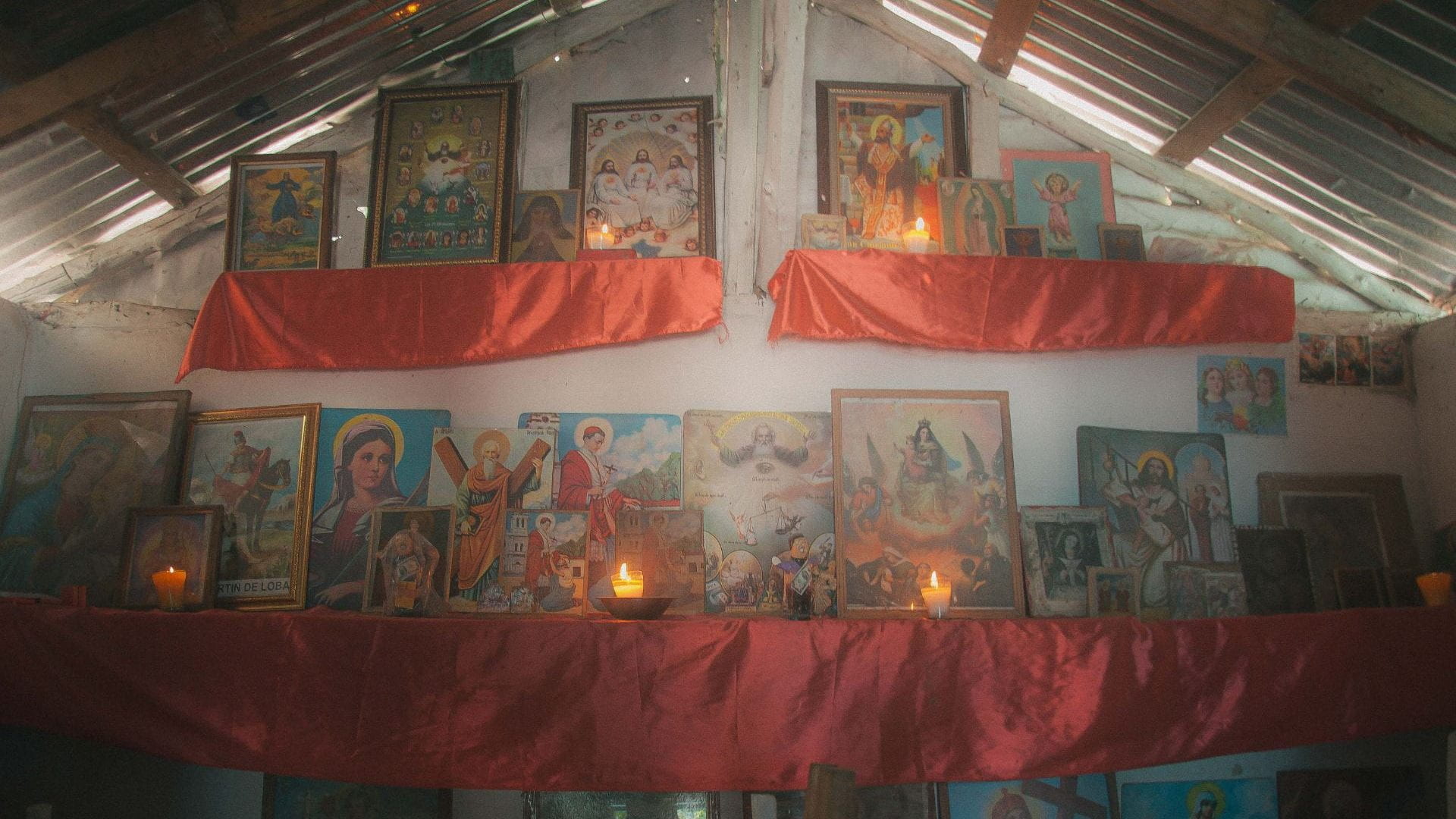An elaborate altar contains various framed images, candles, and silky red fabric.