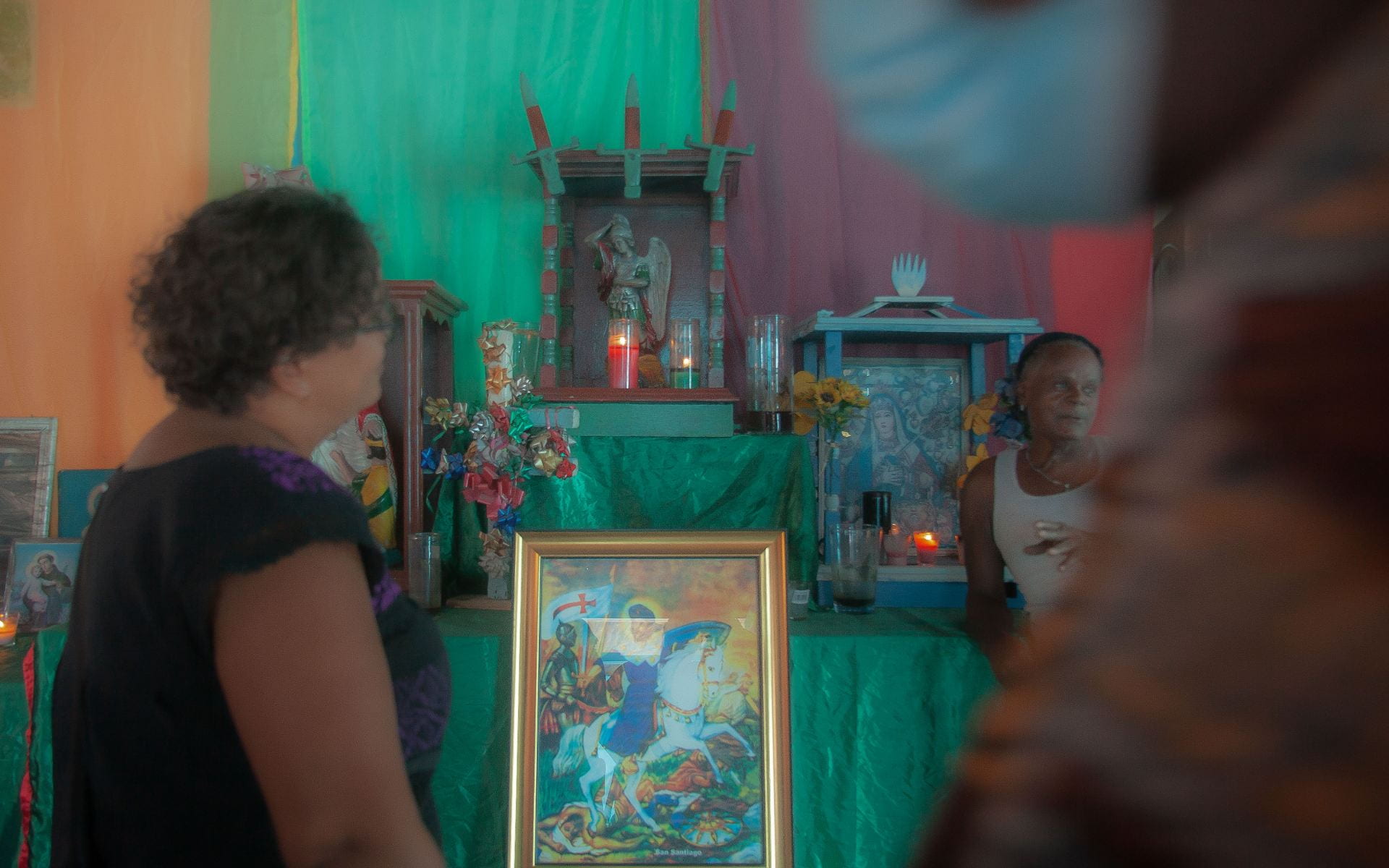 Ana-Maurina Lara stands smiling toward Chimbi, who sits in front of his altar.