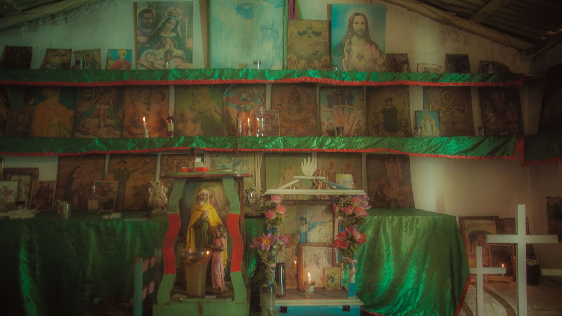 Multiple shelves are lined with shiny green and red fabric, topped with abundant altar items.