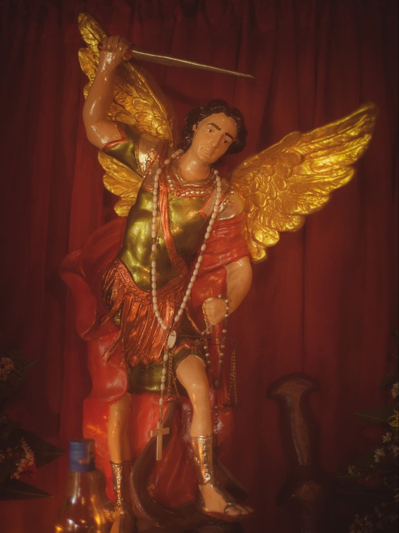 A statue of a masculine figure with gold wings and armor, holding a sword overhead.