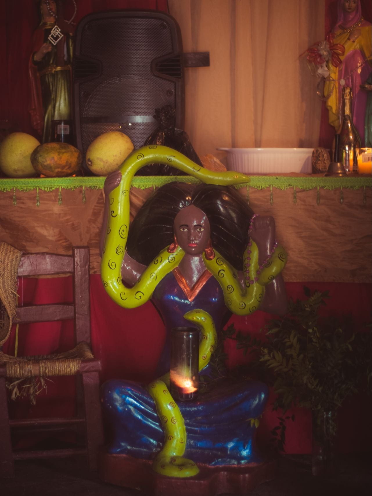 A statue of a feminine figure wearing a shiny blue regal dress and a bright green snake coiled over their body.