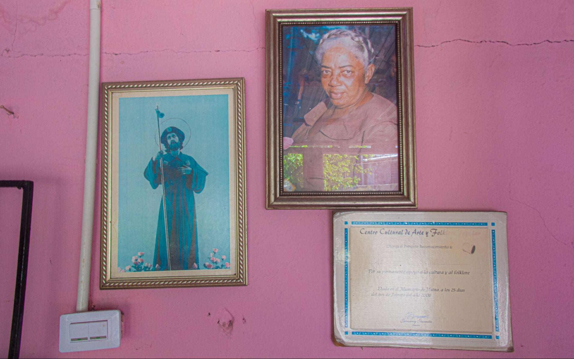 Against a bright pink wall, Graciela's photo, certificate, and a lithograph of Jesus are arranged in frames.