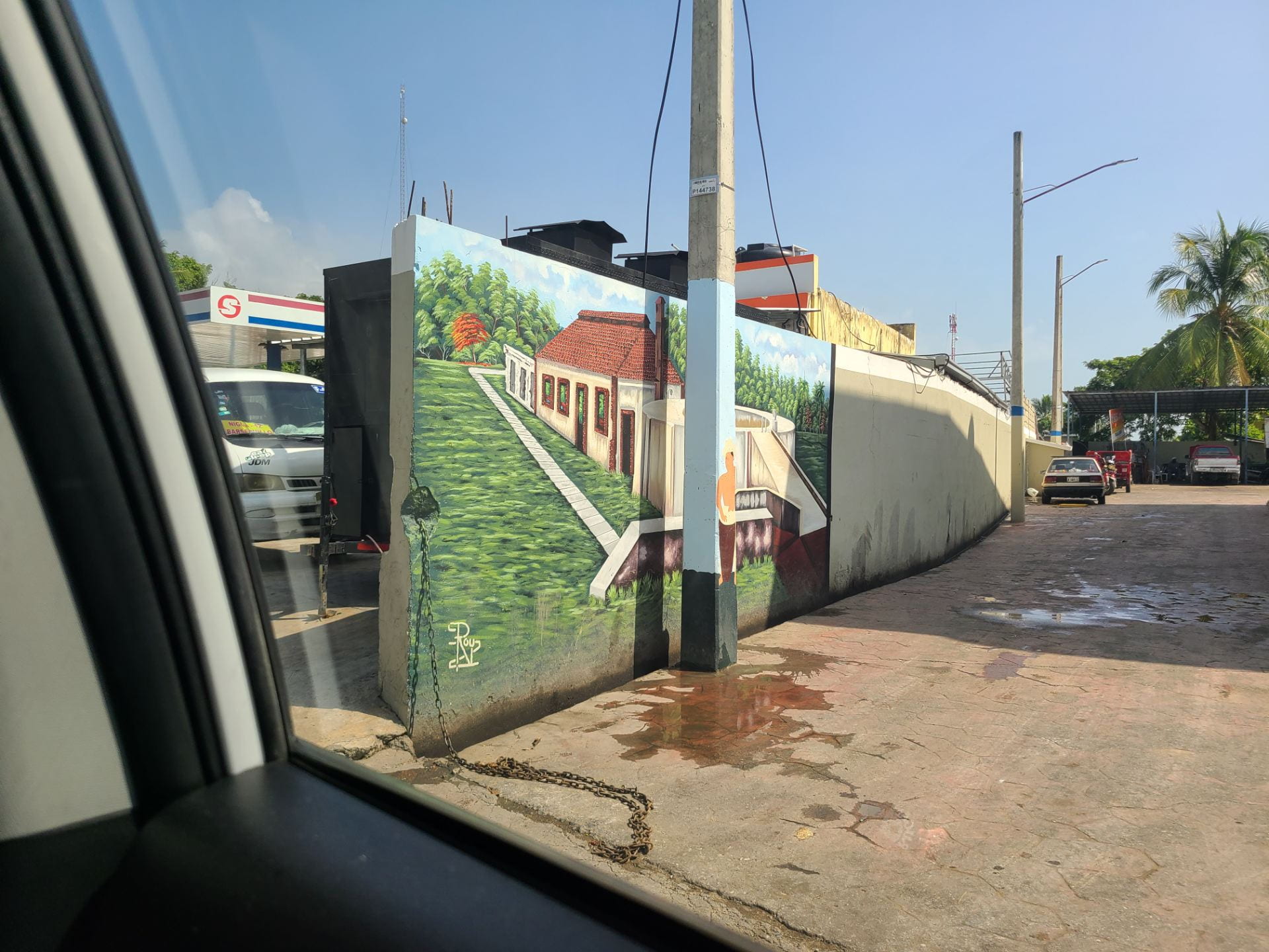 A view from a car window into an alley with a colorful mural depicting a house surrounded by greenery